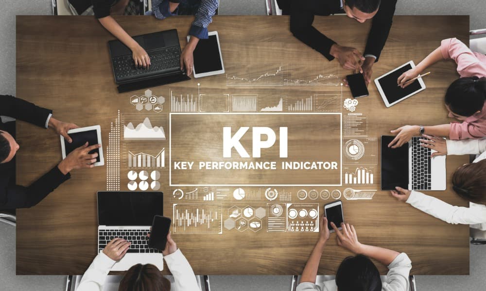 A group of people sitting around a table using laptops and phones to measure KPIs