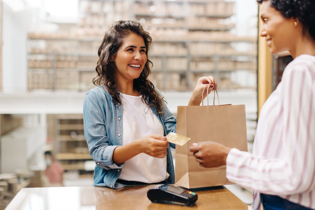 A smiling woman at a checkout counter paying for her purchases with a credit card.