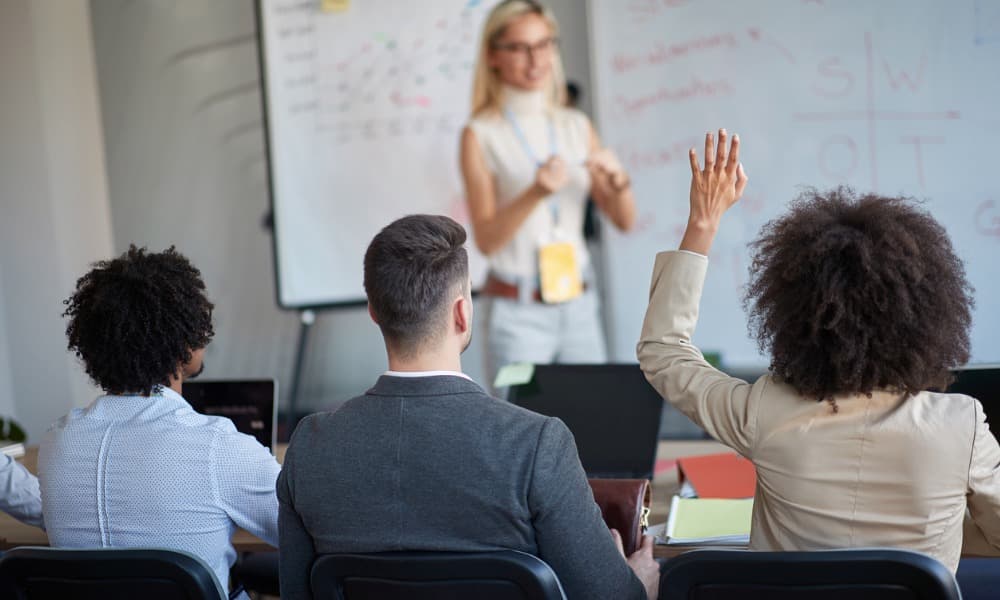 A woman standing in front of a whiteboard addressing a room full of people.