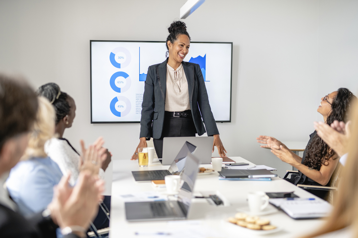 A multi-ethnic diverse group of professionals applaud their leader and discuss how to develop leaders within the company.