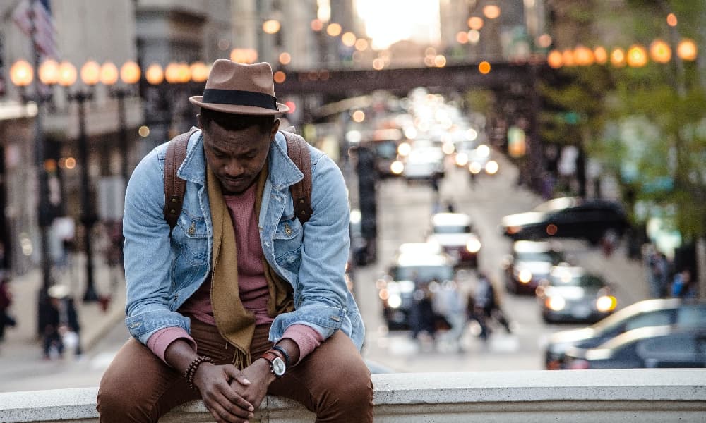 Sad-looking man sitting on railing with a city in the background