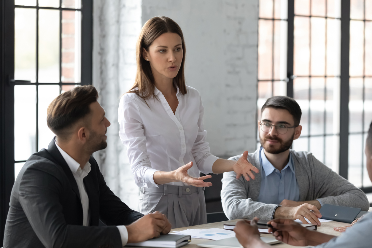 Woman standing up and talking to men sitting down at a table.